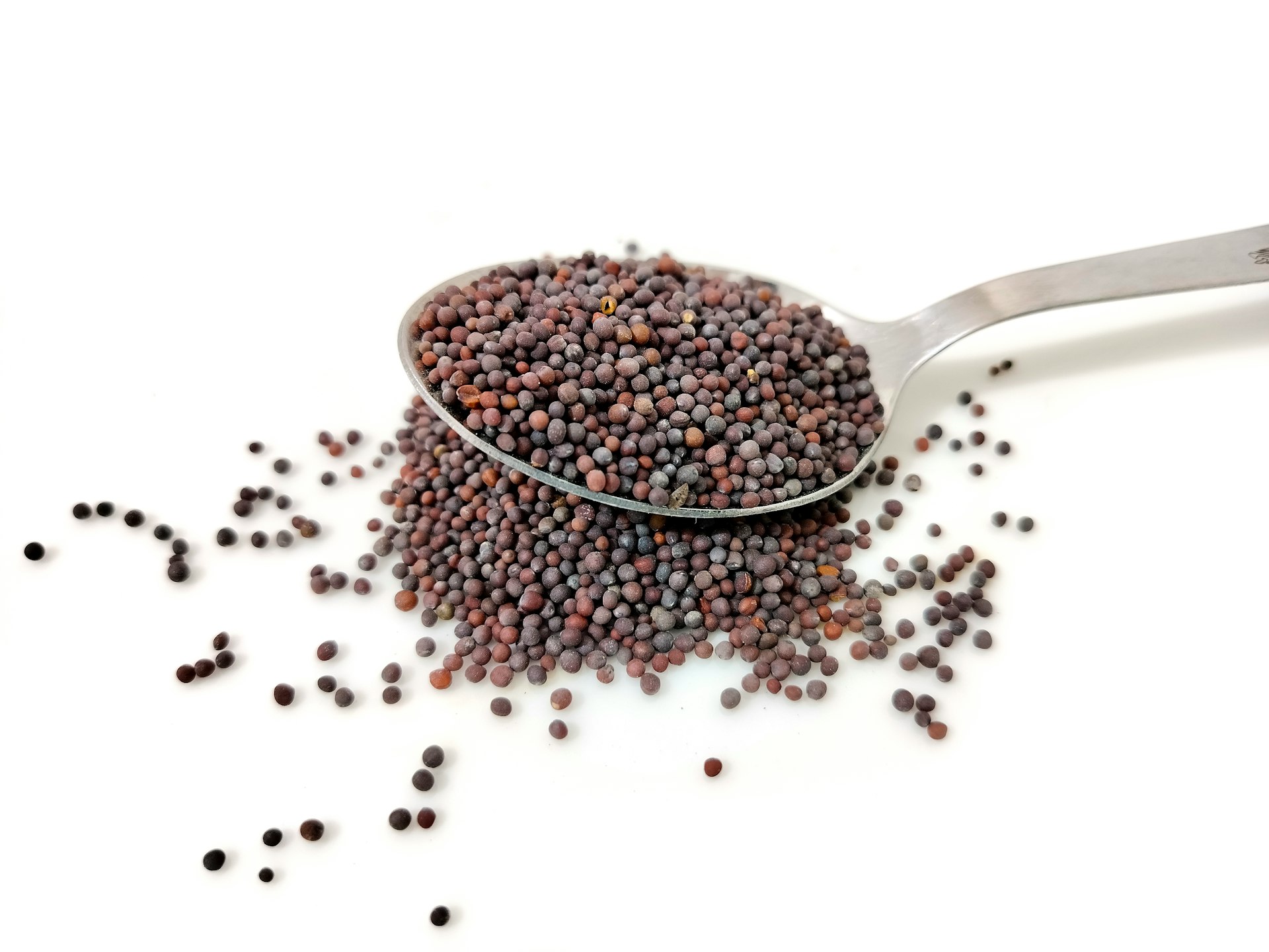 a spoon filled with black seed on top of a white table